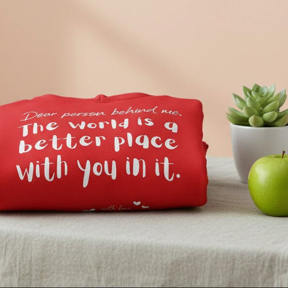Red hoodie with a motivational quote on a table with a glass of water and an apple.